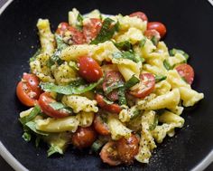 a black plate topped with pasta and tomatoes