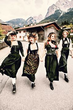 three women dressed in black and white are walking down the street with mountains behind them