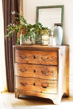 a wooden dresser with plants on top and a mirror in the corner next to it