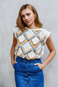 a woman standing with her hands on her hips wearing a crochet top and denim skirt