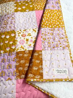 two quilts laying next to each other on top of a white sheet covered in pink, yellow and brown fabric