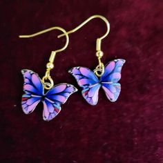 two purple and blue butterflies are hanging from gold earwires on a red velvet surface