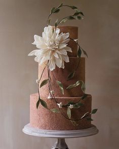 a three tiered cake with white flowers on top and green leaves around the edges