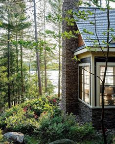 a house in the woods with trees and flowers around it's windows, overlooking water