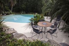 a table and chairs near a pool surrounded by palm trees