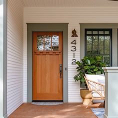 the front door of a house with a chair and potted plant on the porch