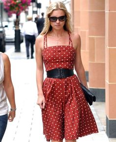 a woman in a red polka dot dress is walking down the street with her hand on her hip