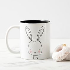 a white and black coffee mug with a donut next to it