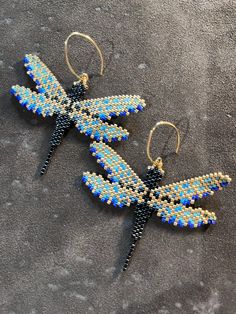 a pair of blue and black beaded dragonfly earrings sitting on top of a gray surface