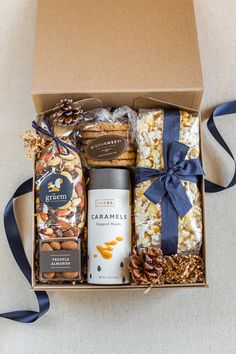 an open gift box filled with nuts, crackers, and chocolates next to a blue ribbon