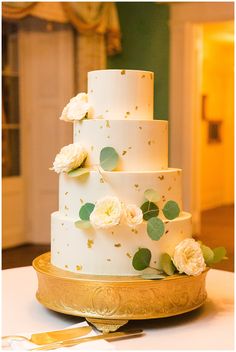 a wedding cake with white flowers and greenery on the top is sitting on a gold platter