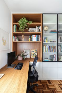 a desk with a laptop computer and bookshelf behind it in front of a window