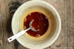 a white bowl filled with sauce on top of a wooden table next to a spoon