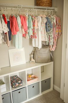 an organized closet with baby clothes hanging on the wall and storage bins below it