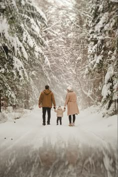 a man and woman walking down a snow covered road holding hands with a child on the other side