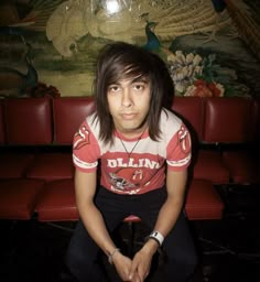 a young man sitting on top of a red couch in front of a wall painting