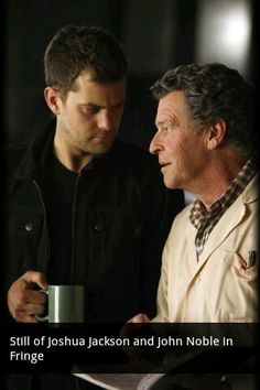 two men standing next to each other with a cup in their hand and one holding a pen