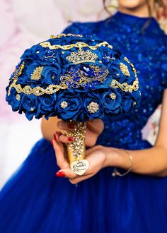 a woman in a blue dress holding a bridal bouquet with gold and crystal accents