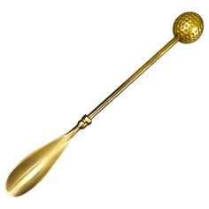 a gold colored metal spoon with a golden ball on the end and a long handle