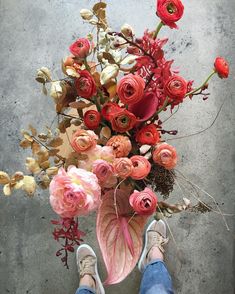 a person standing next to a bunch of flowers on top of a cement floor with their feet propped up