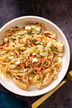 a white bowl filled with noodles and chicken on top of a blue cloth next to a gold spoon