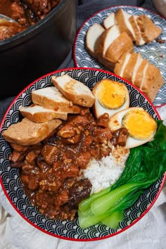 two plates filled with rice, meat and eggs on top of each other next to some bread