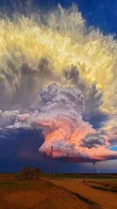 a large cloud is in the sky over a dirt road