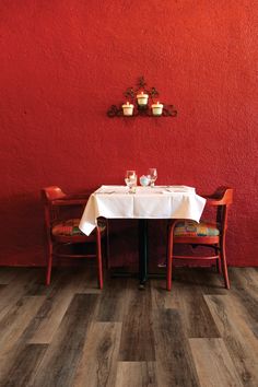 a red wall with two chairs and a table in front of it that has a white table cloth on it