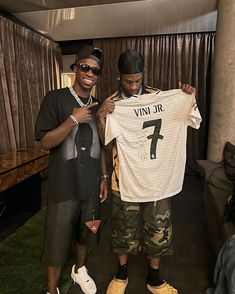 two men standing next to each other holding up a t - shirt with the number seven on it