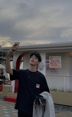 a young man holding up his cell phone in front of a building with an advertisement on it