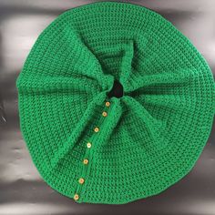 a green crocheted hat with gold buttons on the front and side, sitting on a metal surface