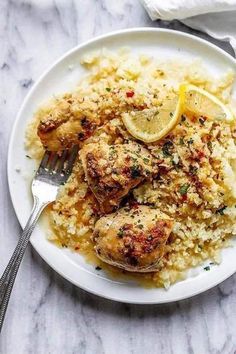 a white plate topped with chicken, rice and lemon wedges next to a fork