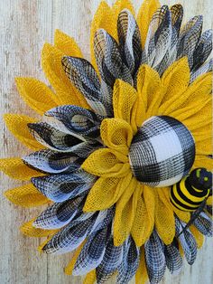 a yellow and black sunflower with a bee on it's head is hanging from a wooden wall