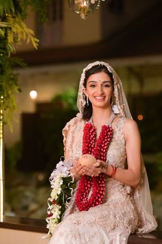 a woman in a wedding dress sitting on a ledge with flowers and beads around her neck