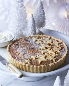 a pie sitting on top of a white plate covered in powdered sugar next to a small christmas tree