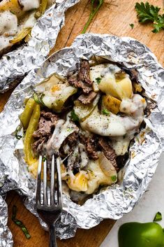 a close up of a plate of food with meat and vegetables on foil wrappers