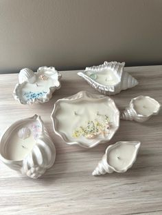 some white dishes sitting on top of a wooden table with seashells in them