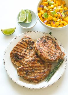 two meat patties on a white plate next to a bowl of mango salsa and lime wedges