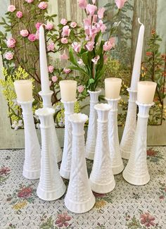 four white candles sitting next to each other on a table with flowers in the background