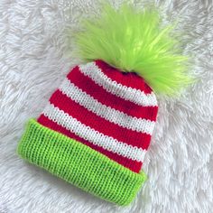 a red and white striped hat with green pom - pom on top sitting on a fluffy white blanket