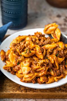 a white plate topped with pasta covered in meat and sauce on top of a wooden cutting board