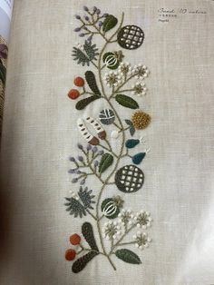 an embroidered design with flowers and other things on the side of a piece of cloth