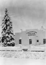 an old black and white photo of a snow covered tree in front of a police station