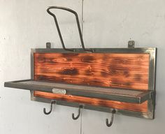 a metal and wood shelf with hooks hanging from it's sides on a wall