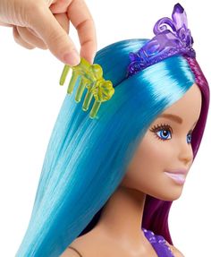 a barbie doll with blue and purple hair is being combed by someone's hand