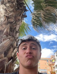 a man standing in front of a palm tree looking up at the camera and making a funny face