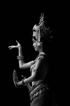 a woman dressed in an elaborate costume and headdress is standing with her hands out