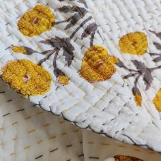 a close up of a quilt on a bed with yellow and brown flowers in it