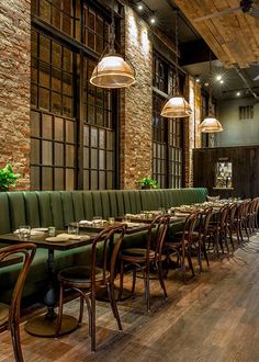 an empty restaurant with green booths and wooden tables in front of large windows, hanging lights above them