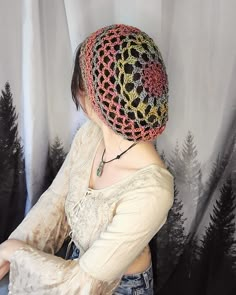 a woman wearing a crochet hat with trees in the background and curtains behind her